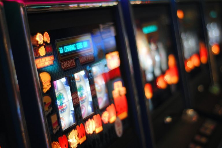 A lineup of slightly out-of-focus pokie machines is visible.
